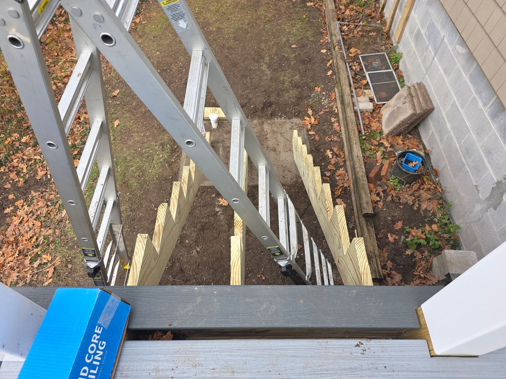 View from a balcony over a narrow alley with a ladder, fence, and scattered leaves below