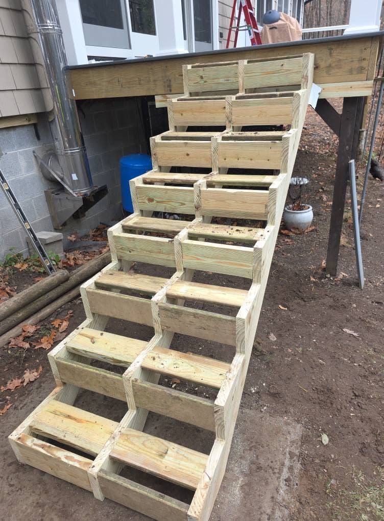 Wooden outdoor staircase under construction, with unfinished steps leading up to a raised deck.