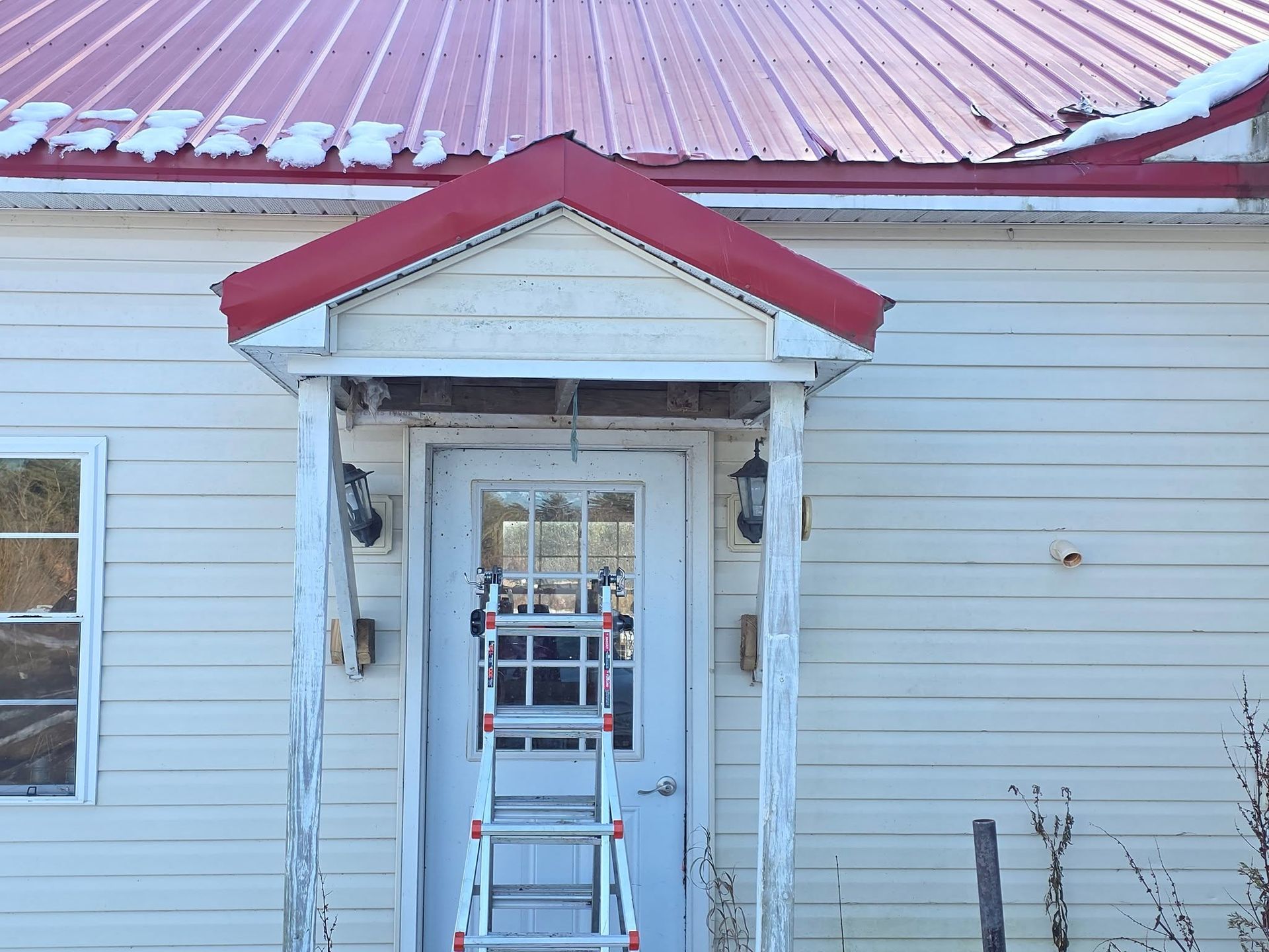 Front porch with a ladder under a small red-trimmed awning on a white house