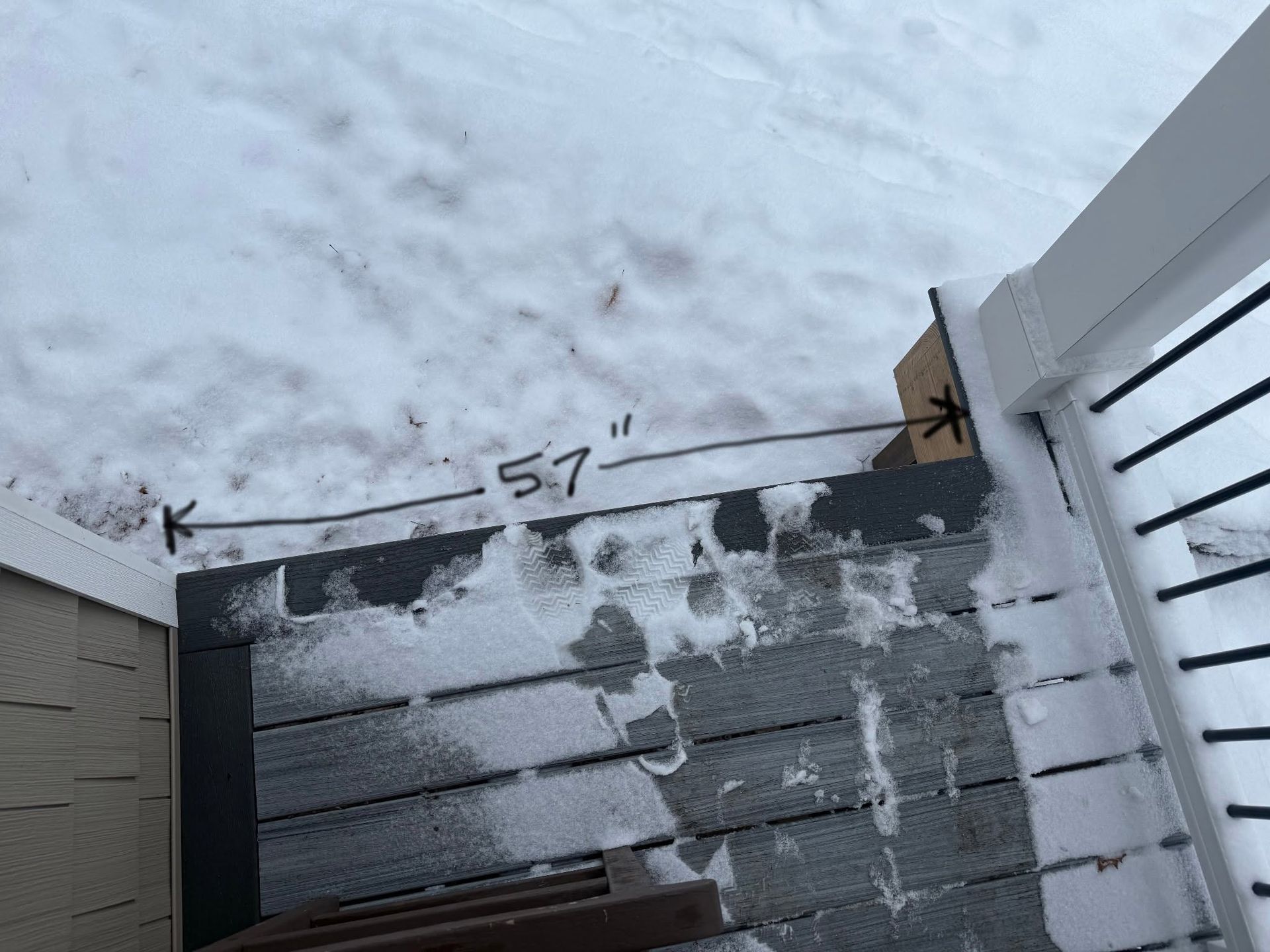 Snow-covered backyard fence and wall marked with a 57-inch measurement line