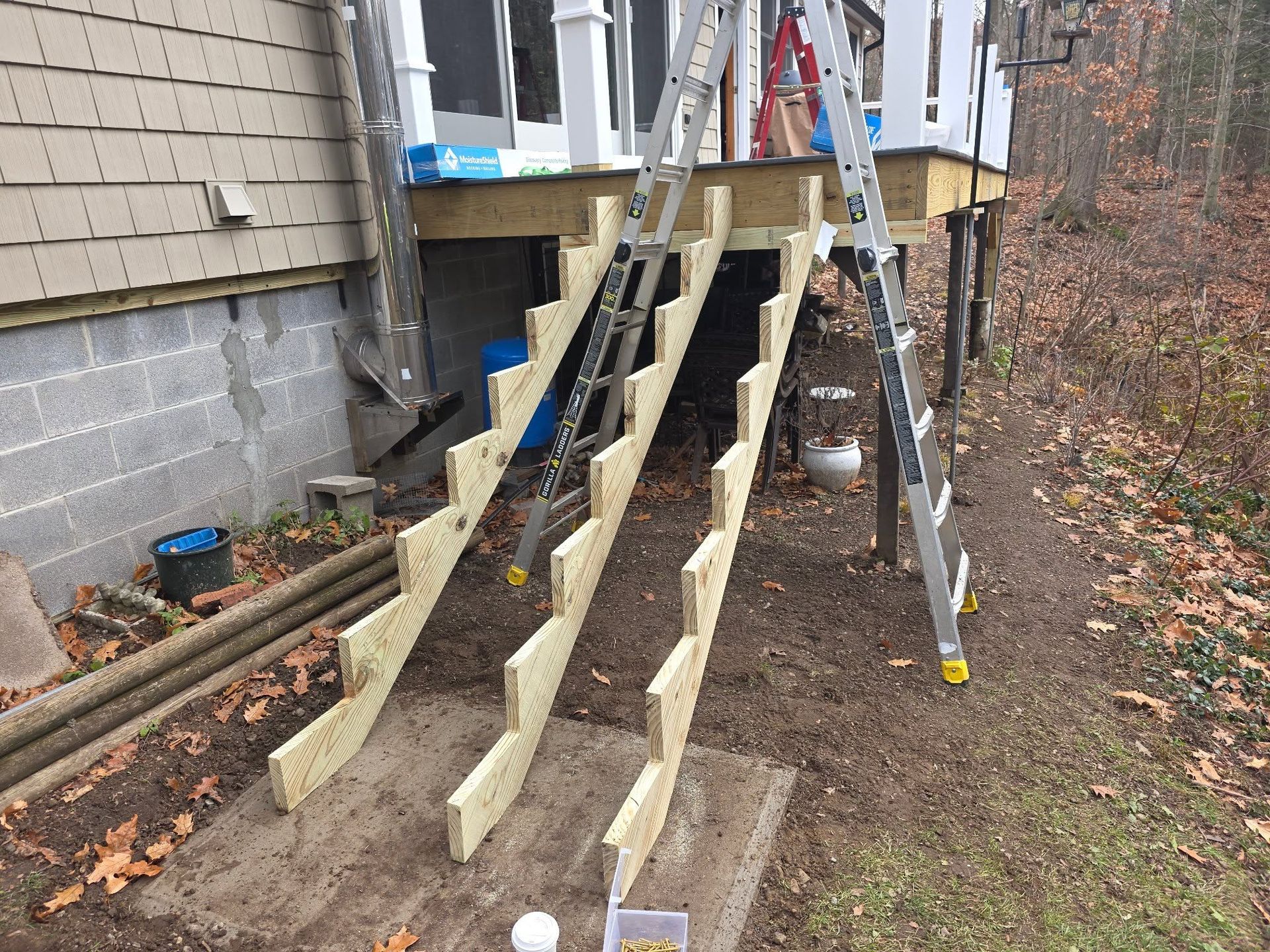 New wooden stairs under construction beside a house, with tools and ladders in a yard