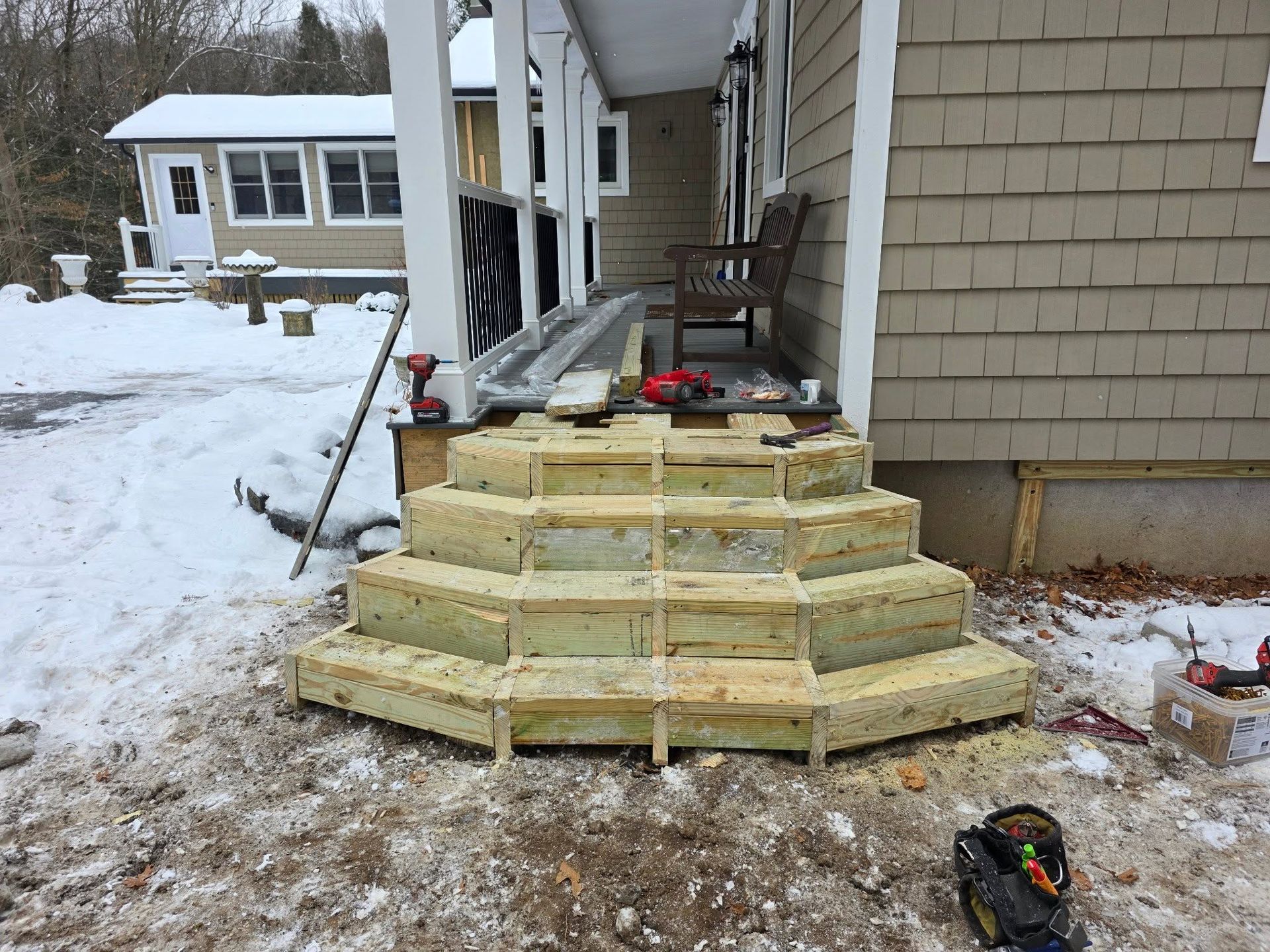 Snowy front porch with newly built wooden steps under construction at a house
