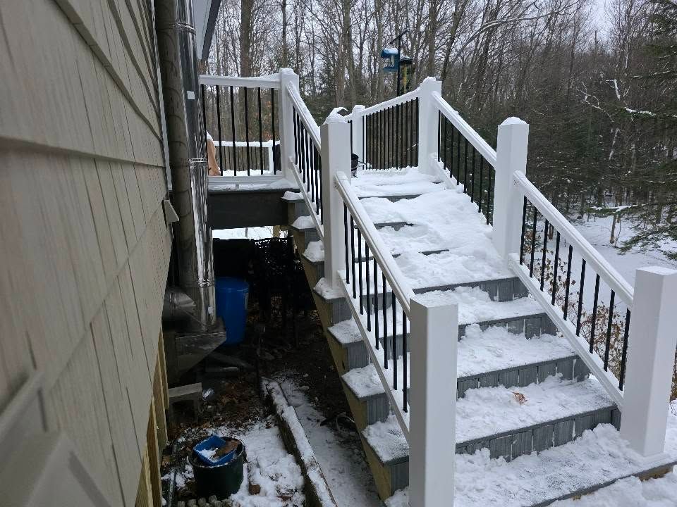Snow-covered wooden stairs and deck beside a house, leading down to a yard.