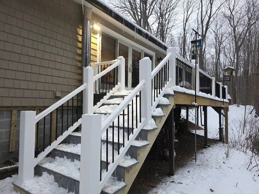 Snow-covered back deck stairs with white railings beside a house at dusk