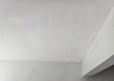 White ceiling corner with a beam and plain light-gray walls indoors