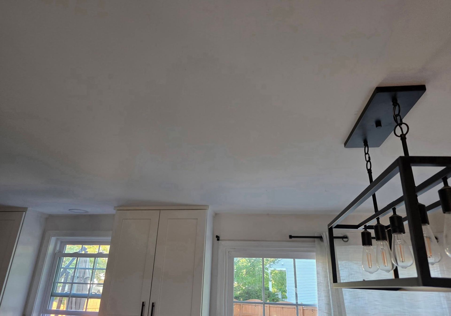 Interior room with white ceiling, windows, and a black hanging light fixture above a bed