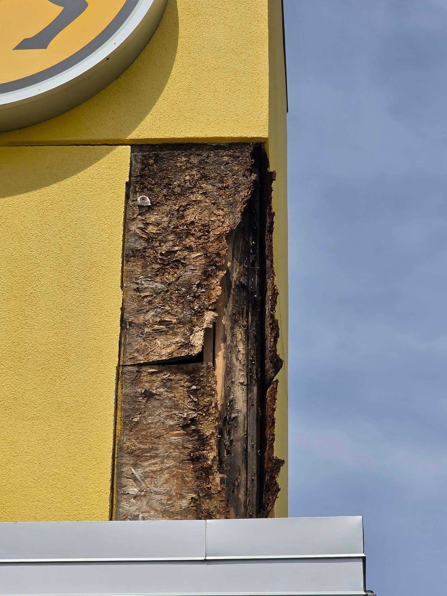Close-up of damaged yellow wall with exposed insulation and peeling material near a window edge