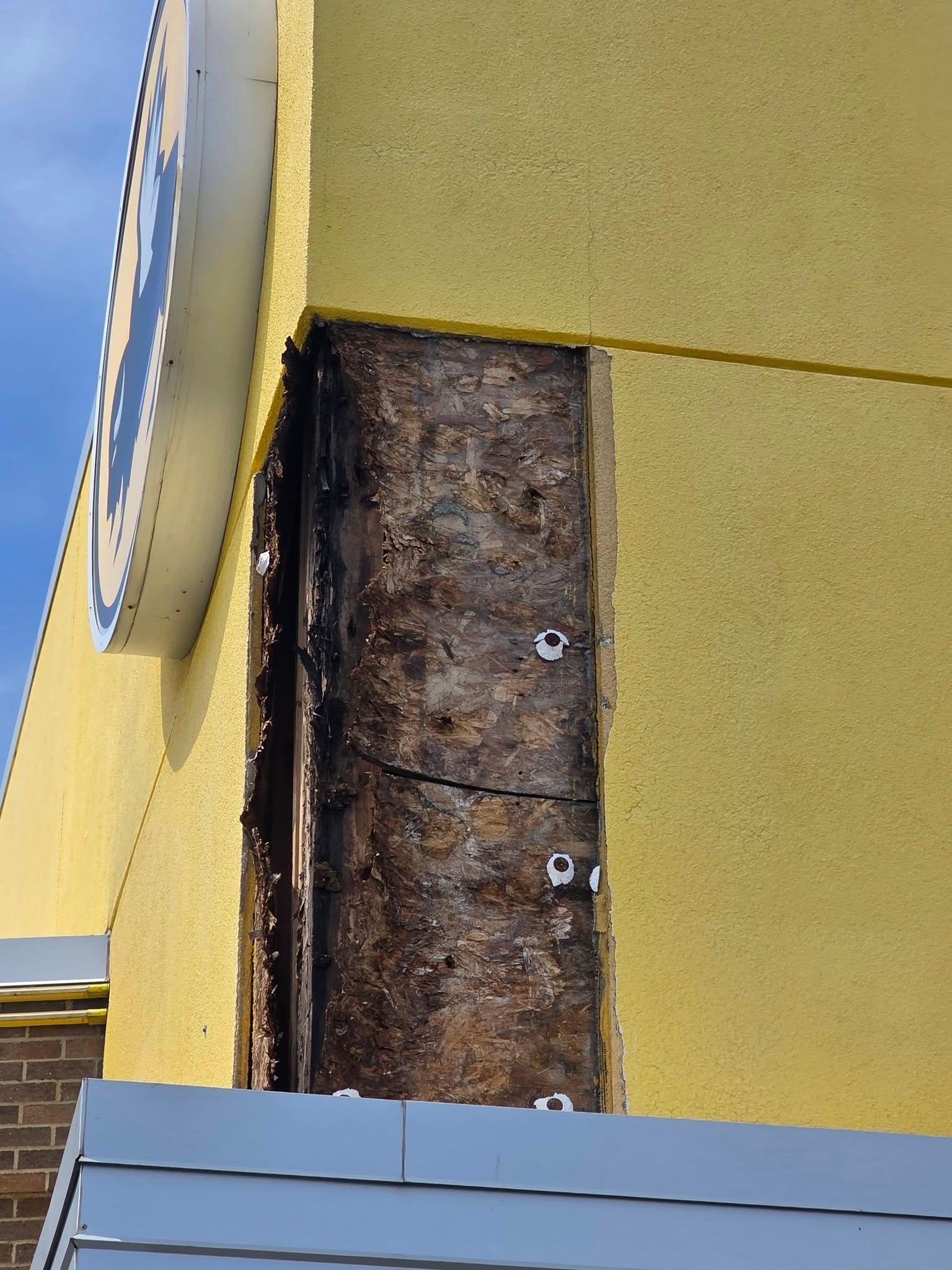 Yellow exterior wall with a vertical exposed, weathered section and a partial sign on the left