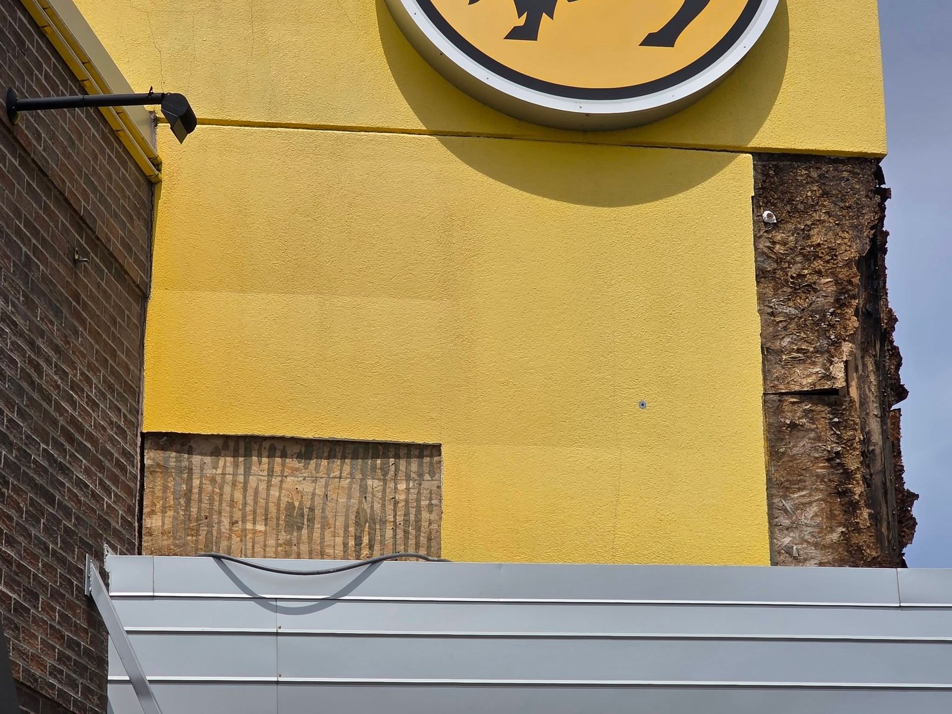 Yellow building wall with a round sign above a gray metal barrier and a rough brick edge