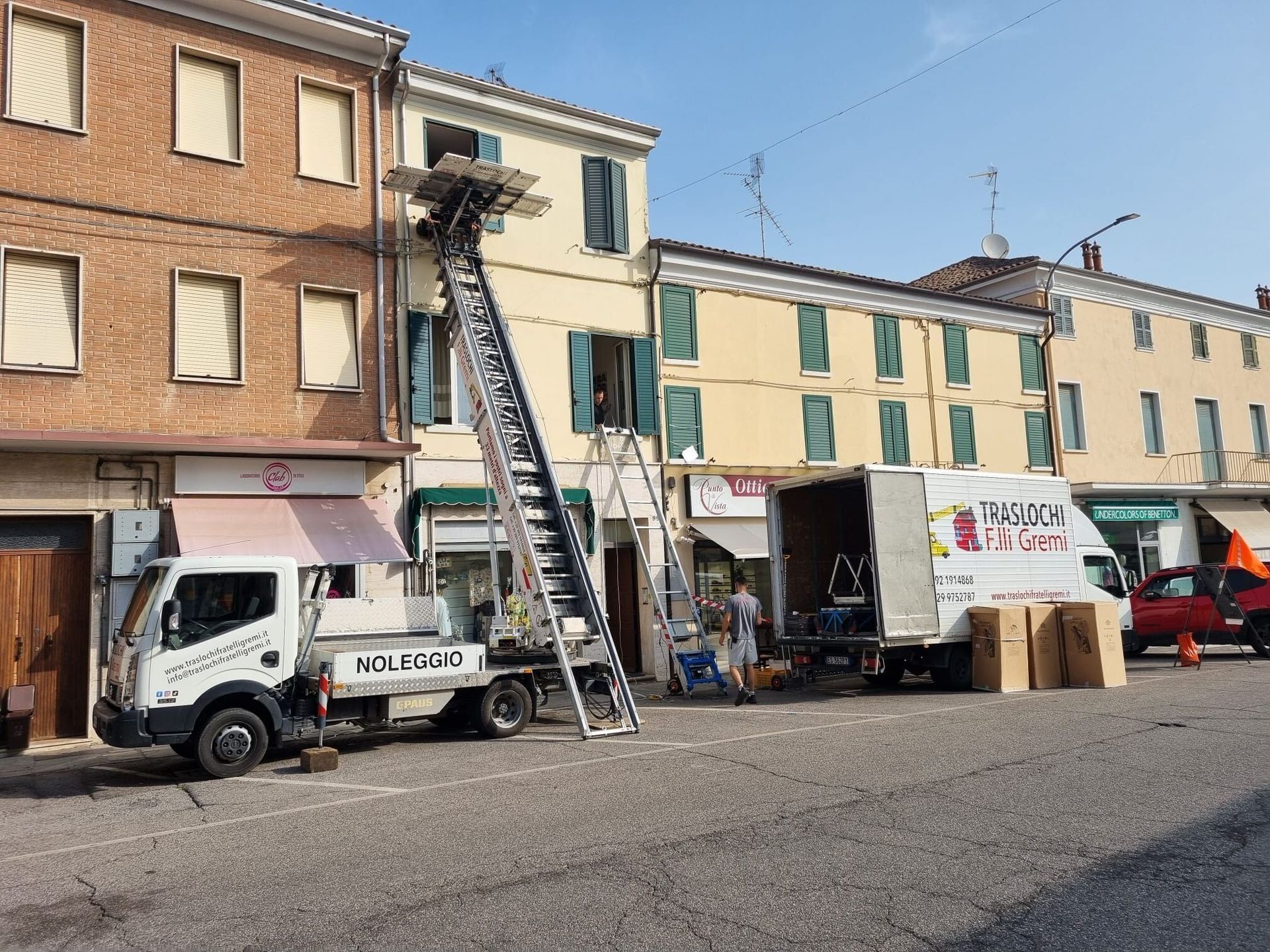 Alcuni operai su una scala riparano la facciata di un edificio accanto a un camion bianco in strada.