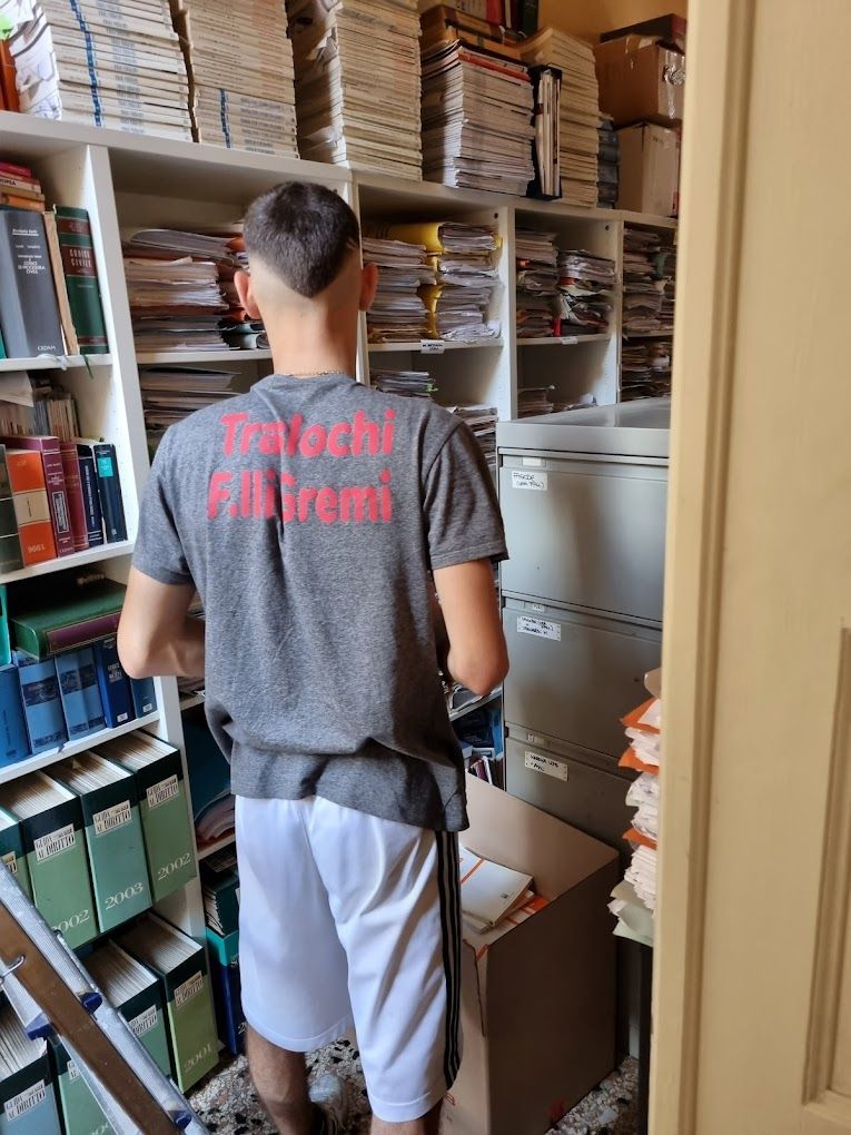 Una persona che smista documenti in un affollato ripostiglio d'ufficio, vista di spalle.