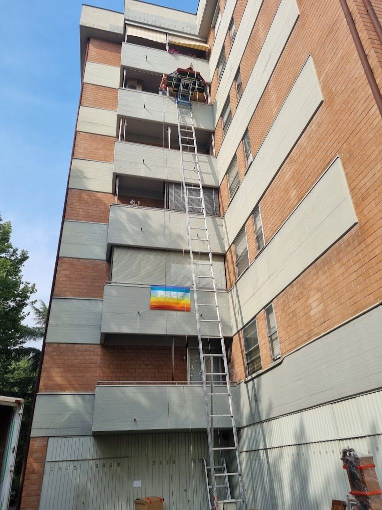 Operai su una scala sospesa accanto a un condominio in mattoni, probabilmente impegnati in lavori di manutenzione esterna.