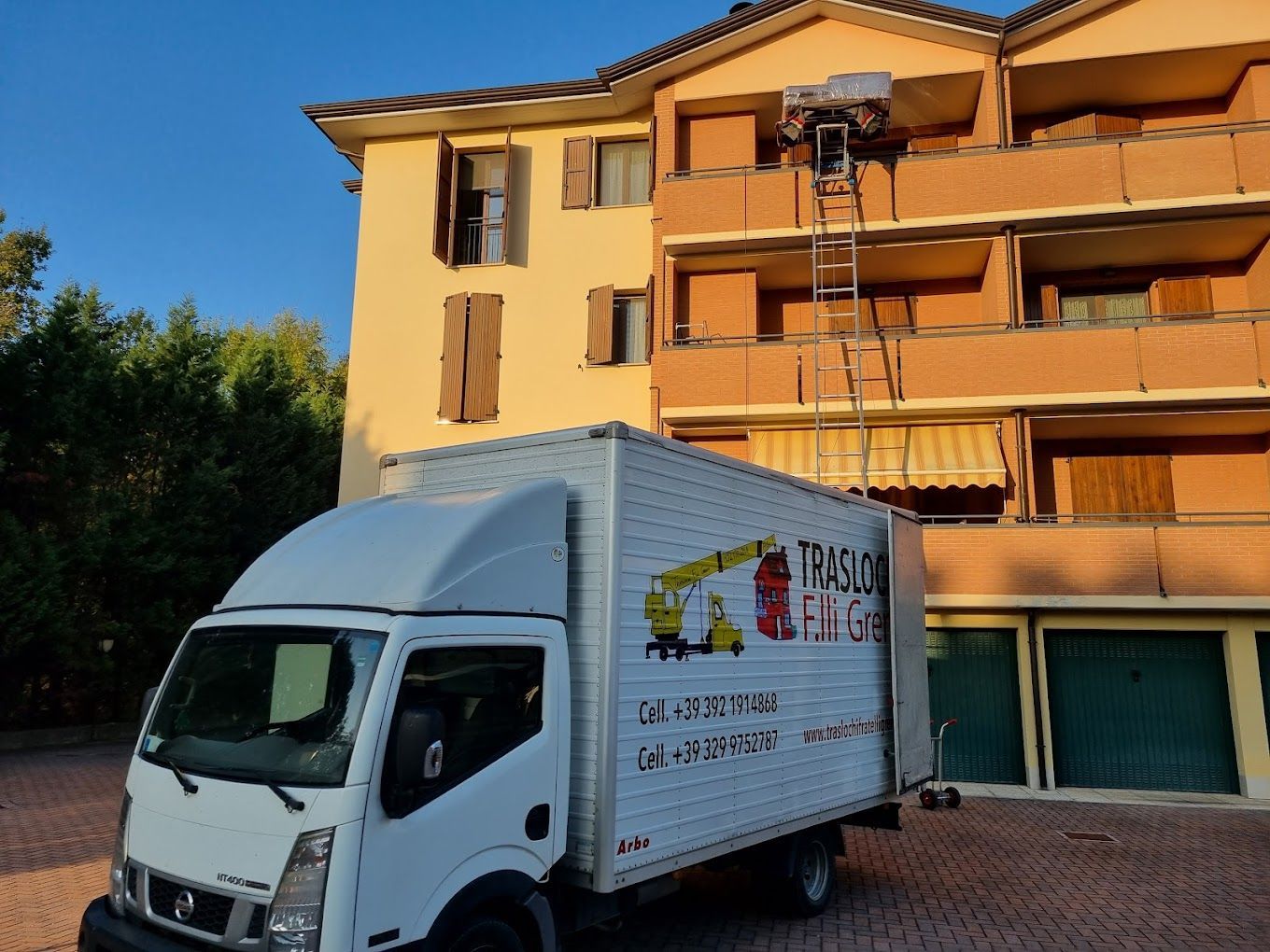 Un furgone bianco per le consegne è parcheggiato davanti a un palazzo giallo con una scala sulla facciata.