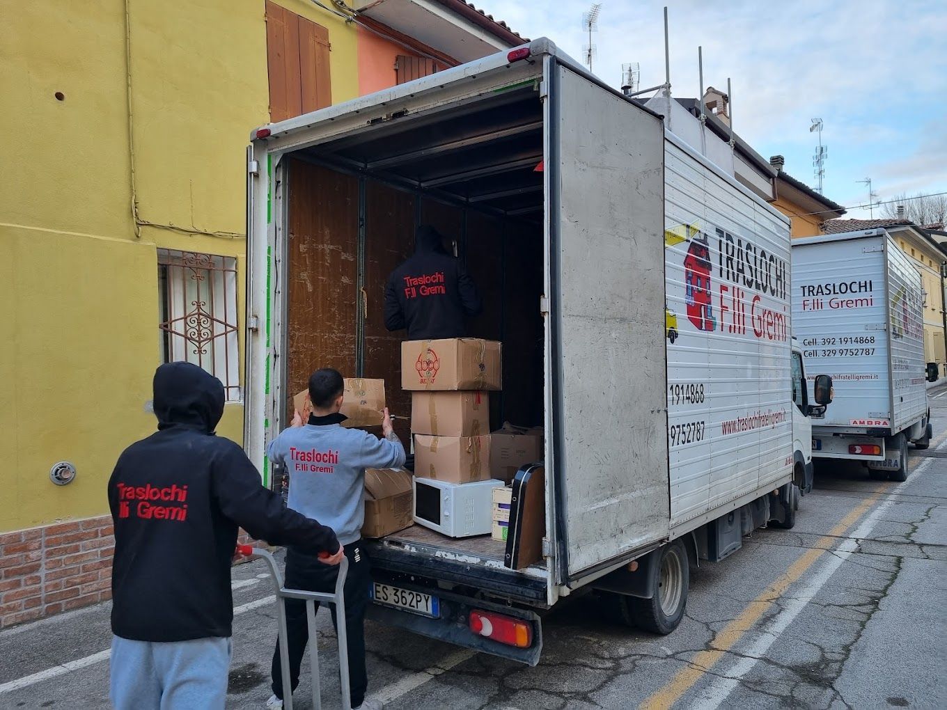 Persone che caricano scatole di cartone su un camioncino bianco per le consegne in una strada cittadina