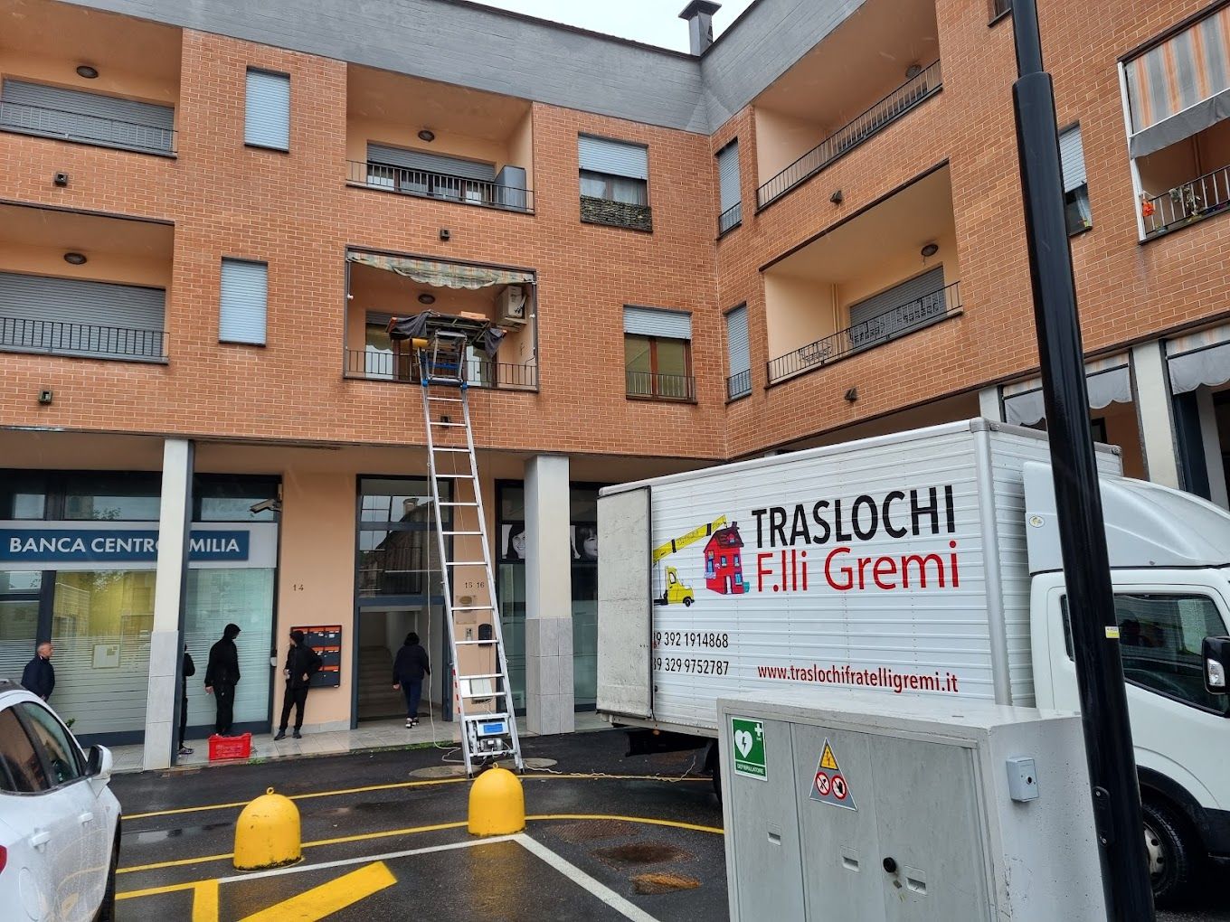 Camion dei traslochi e scala fuori dal cortile di un condominio in mattoni.