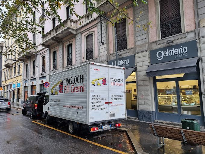 Camion delle consegne parcheggiato su una strada cittadina bagnata, accanto a vetrine e una panchina.