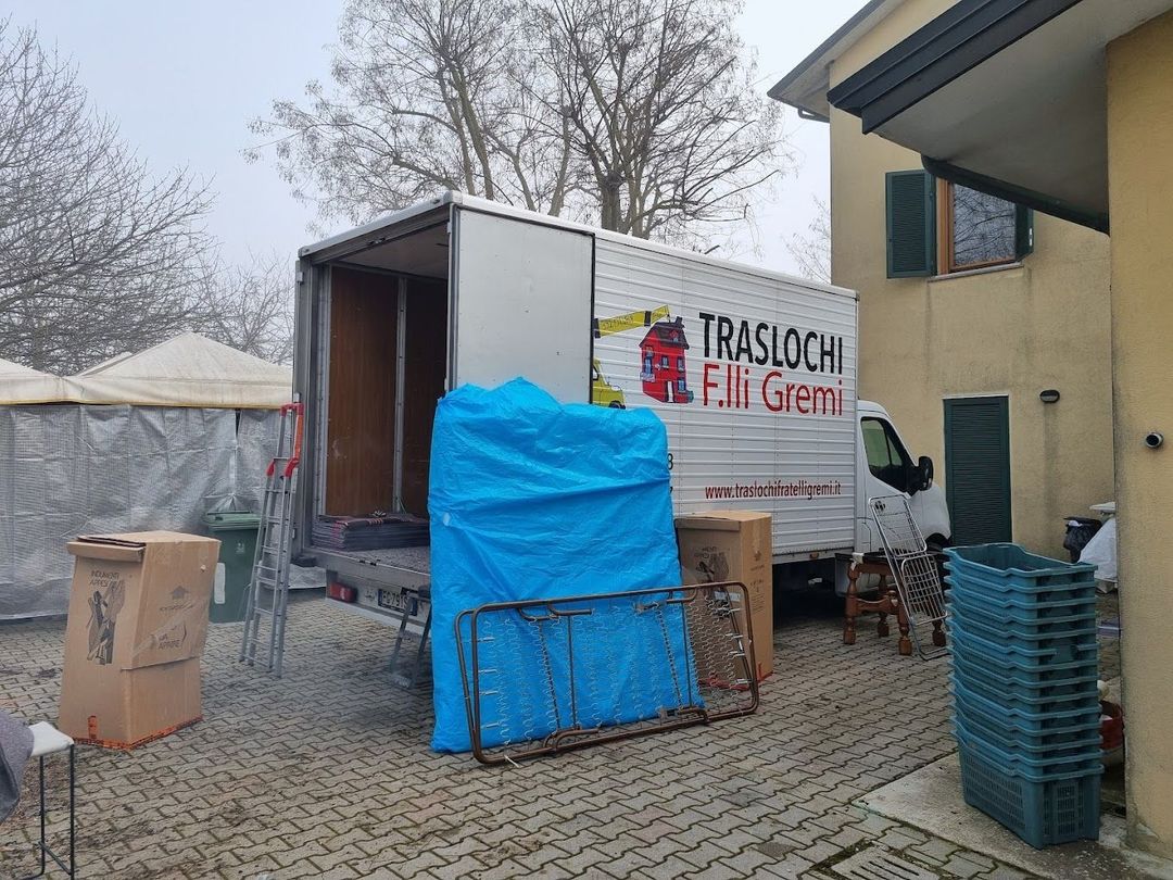 Un camion per traslochi scarica scatole e mobili imballati in un cortile adiacente a una casa.