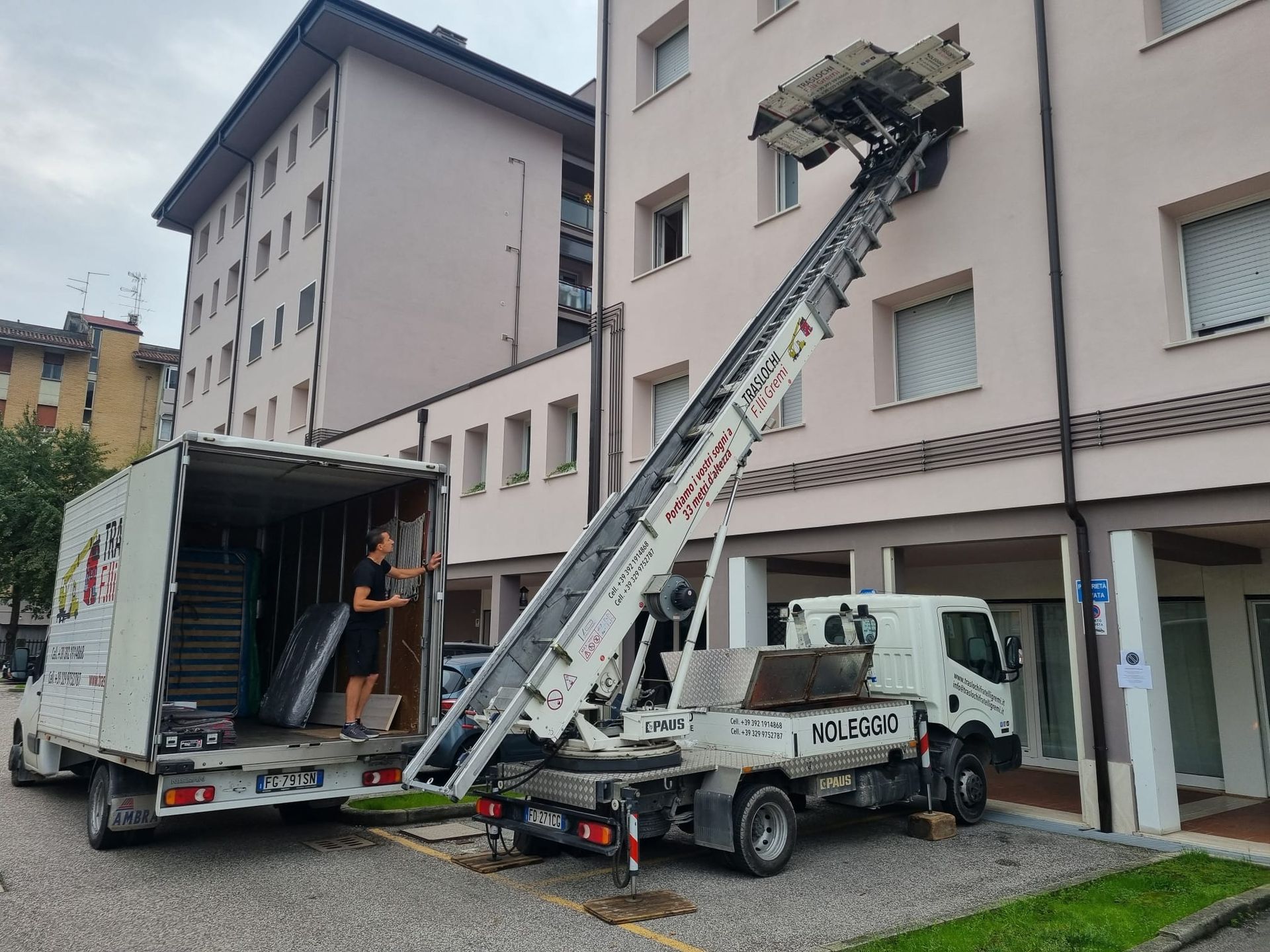 Un camion per traslochi scarica mobili con una gru accanto a un condominio.