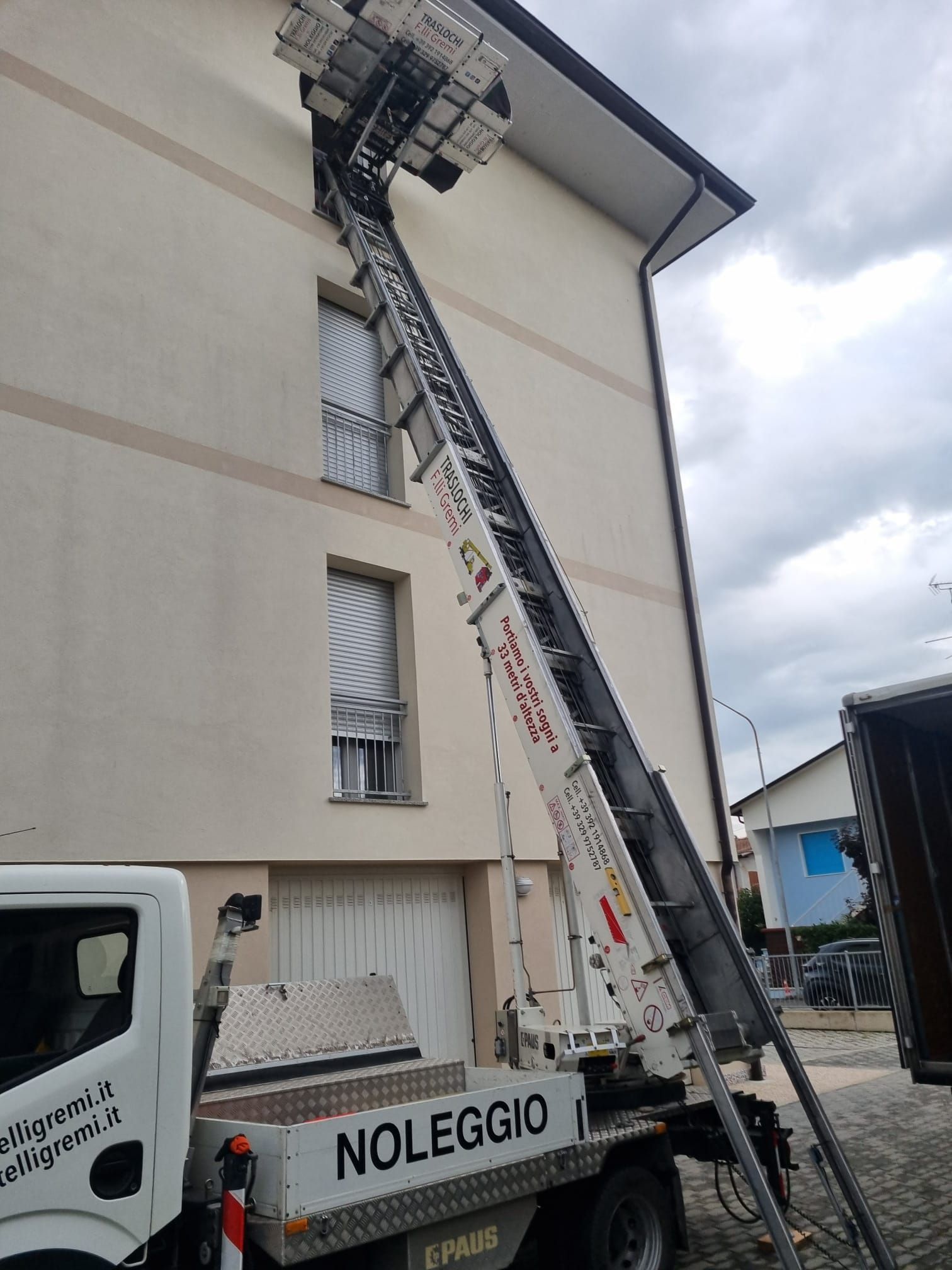 Scala montata su camion che raggiunge il tetto di un edificio per lavori esterni, con un camion a noleggio