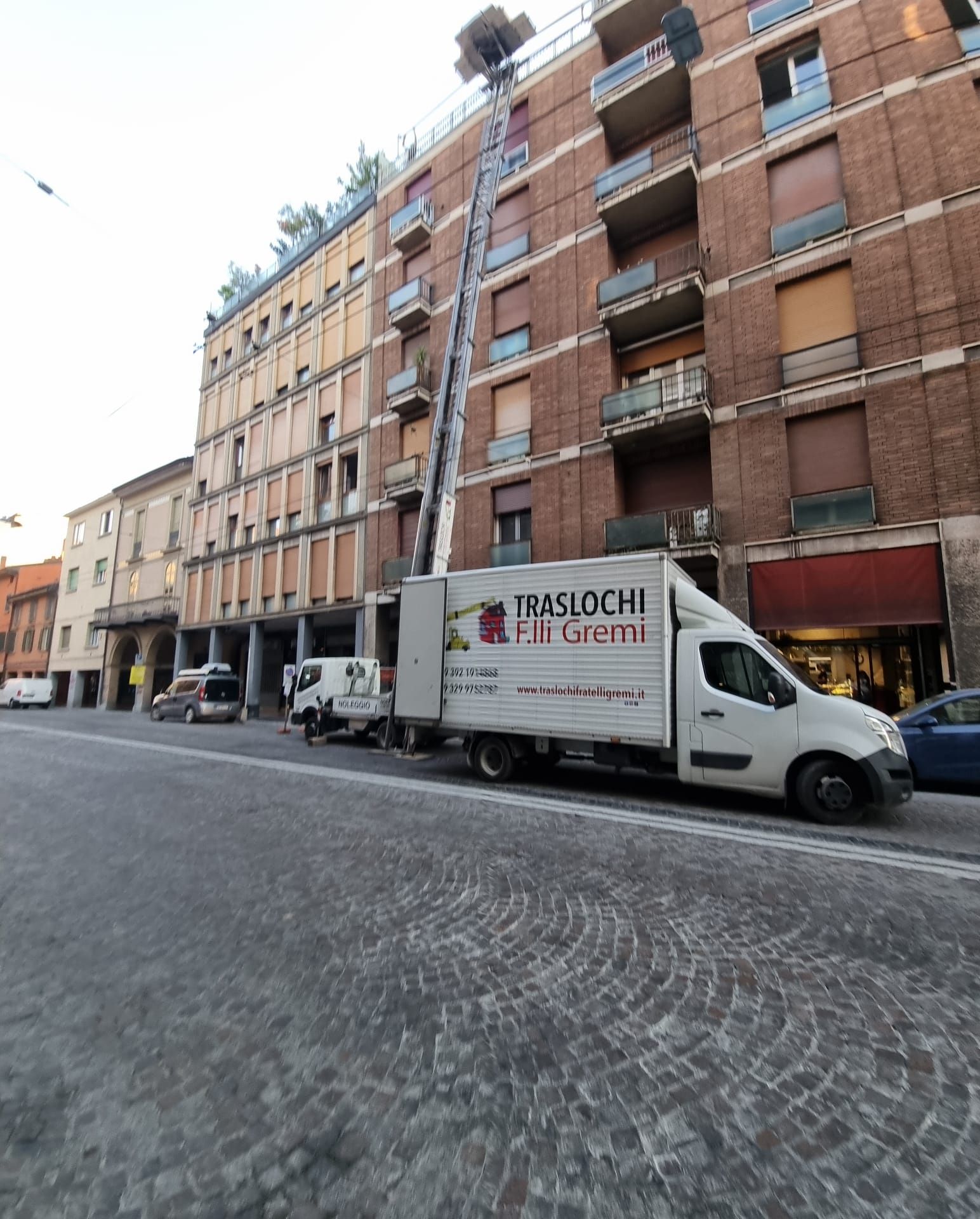 Strada con palazzi in mattoni e un furgone bianco per le consegne parcheggiato sul selciato.