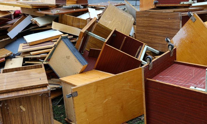Mobili e cassetti di legno rovesciati e sparsi in una stanza interna disordinata con pavimento in legno.