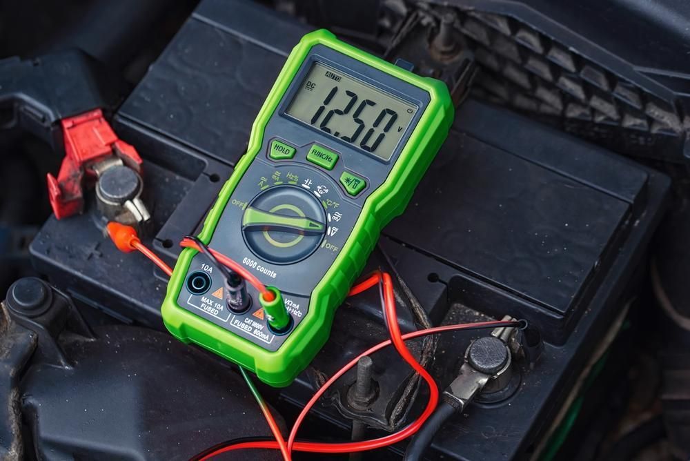A Digital Multimeter Is Sitting on Top of A Car Battery — Envy Automotive in Gorokan, NSW