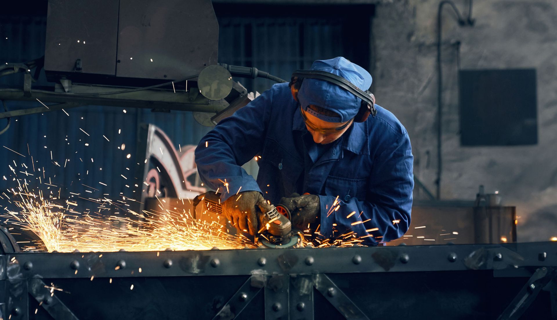 Welder in blue coveralls grinding metal, sparks flying — Envy Automotive in Gorokan, NSW