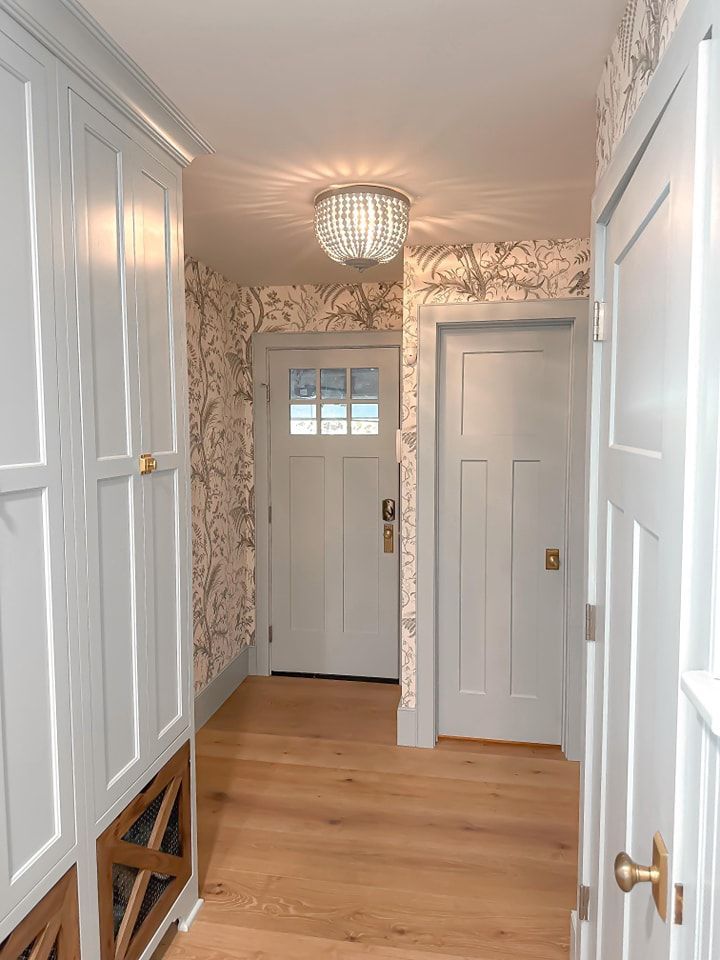Hallway with light blue doors, cabinets, and a chandelier; floral wallpaper and wooden floors.