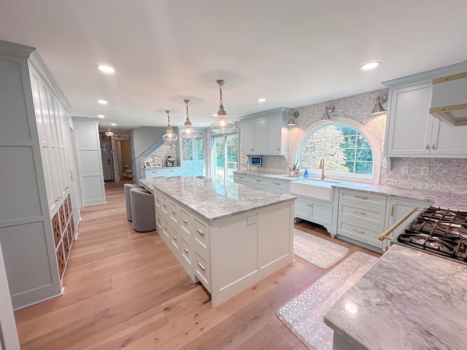 Spacious kitchen with a light blue island, white cabinets, and wood flooring.