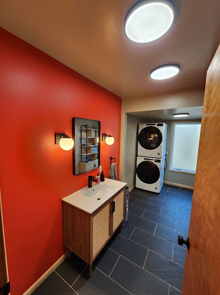 Red-walled laundry room with a vanity, stacked washer/dryer, and overhead lights.
