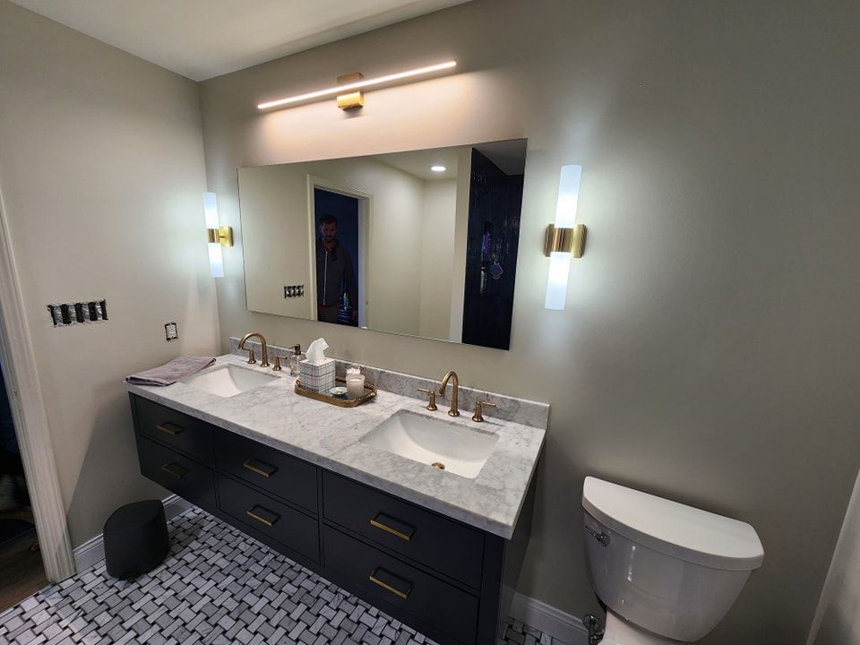 Modern bathroom with floating navy vanity, marble countertop, gold fixtures, and grey walls.