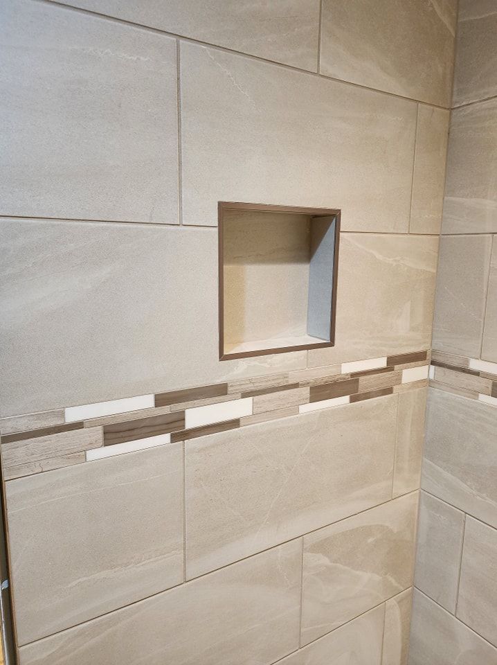 Bathroom corner with beige tile, a recessed shelf, and decorative tile accent.