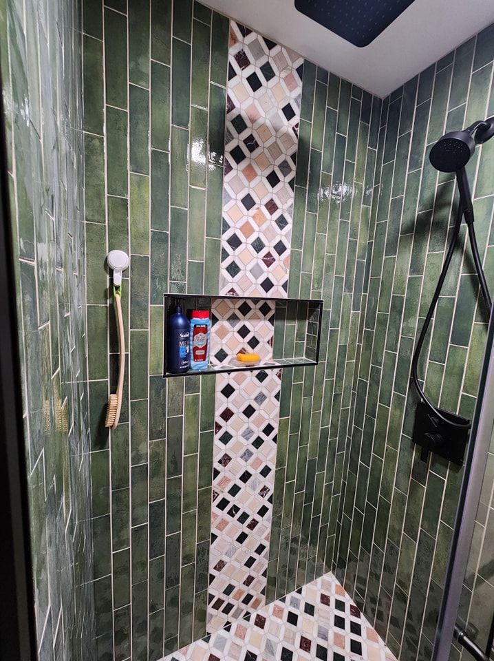 Green tiled shower with a decorative mosaic stripe and built-in shelf.