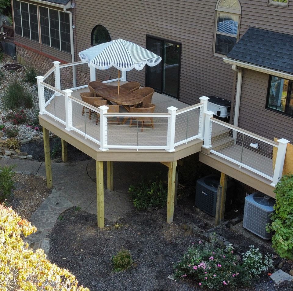 Elevated deck with white railing, beige deck boards, table and chairs, and a striped umbrella.
