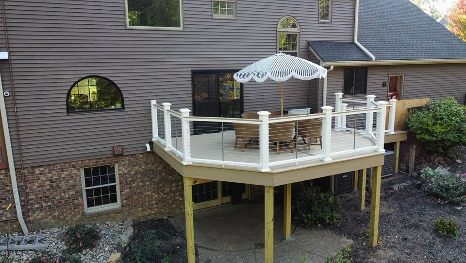 Deck with white railing, glass panels, and umbrella; attached to a house with siding and windows.