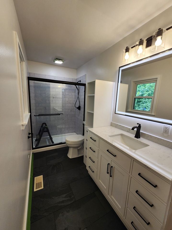 Bathroom with black floor, white vanity and shower, and large mirror.