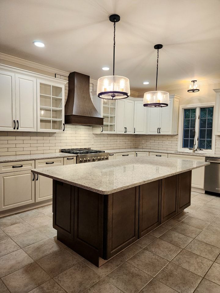 Kitchen with white cabinets, dark island, range hood, and pendant lights.