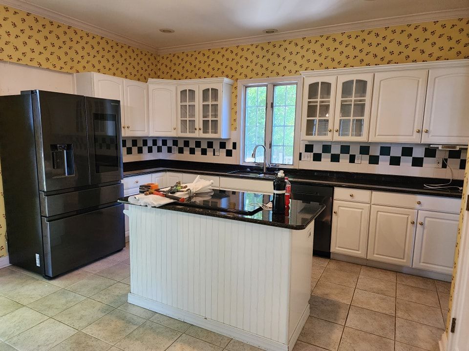 Kitchen with white cabinets, black countertops, and a black island. Black refrigerator and yellow patterned wallpaper.