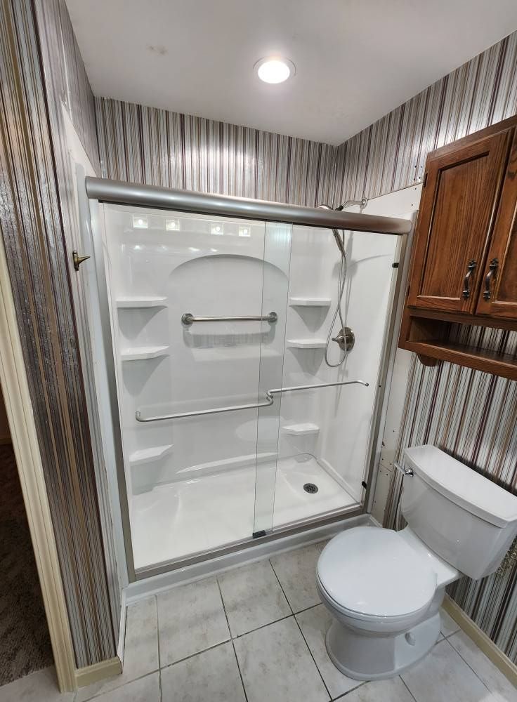 Bathroom with a white shower, toilet, and wooden cabinet, against striped wallpaper.