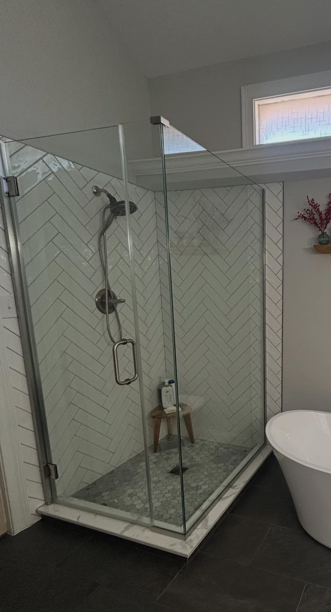 Modern bathroom with glass shower, white herringbone tile, and a freestanding tub.