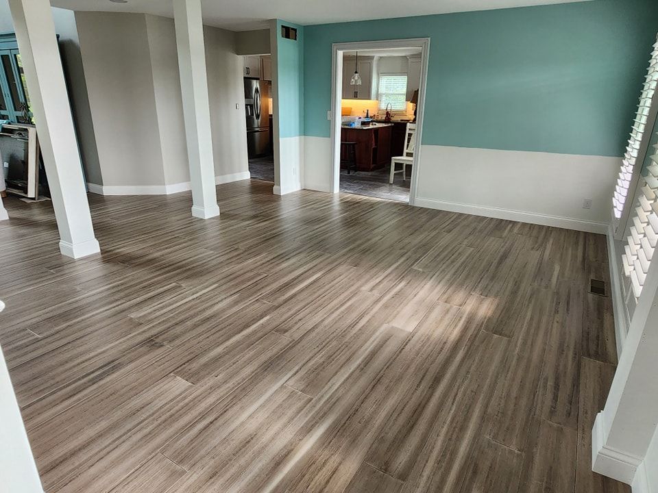 Newly installed wood-look floor in a room with white columns, turquoise and white walls, and an adjacent kitchen.