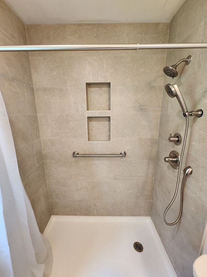 Accessible shower with grab bar, built-in shelving, and handheld showerhead. Beige tile and white shower base.