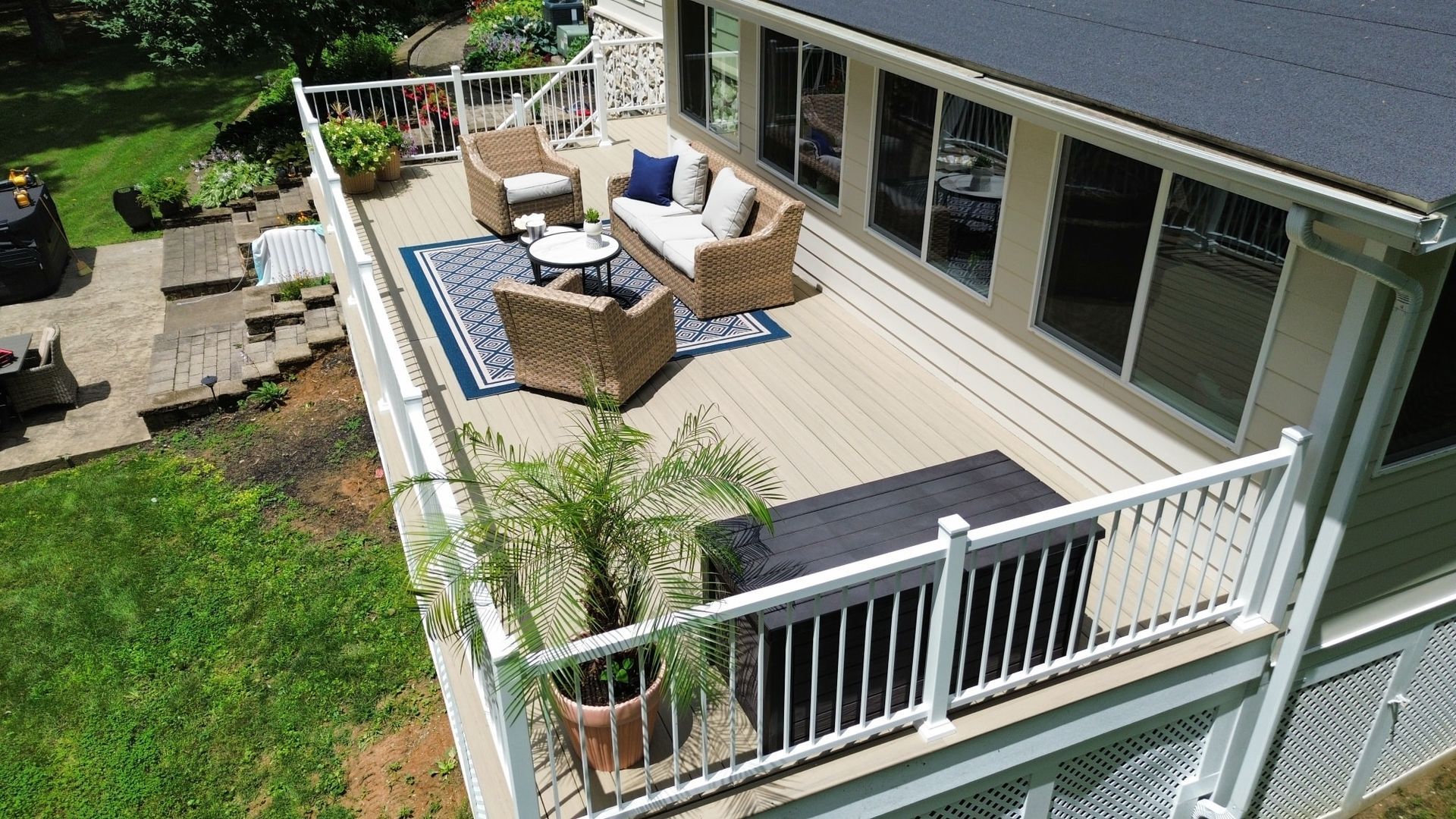 Outdoor deck with wicker furniture, a blue rug, and potted plants.
