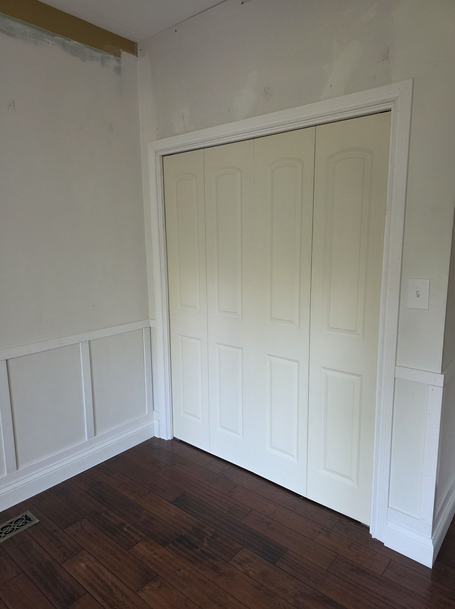 Closet with bi-fold doors, white trim, and paneling. Brown floors, beige doors, white walls.