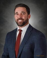 Man in blue plaid blazer, red tie, smiling; against gray background.