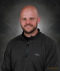 Bald man with a beard in a gray long-sleeved shirt, smiling in front of a gray backdrop.