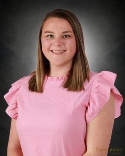 Woman in pink ruffled top smiles, posing in front of a graduated gray background.