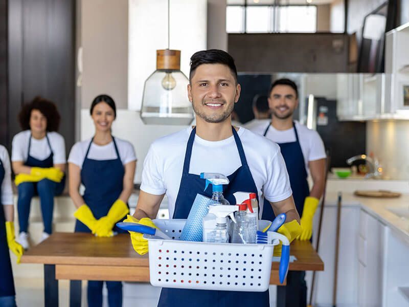 Cleaning crew smiling in a modern kitchen, carrying supplies in a basket.