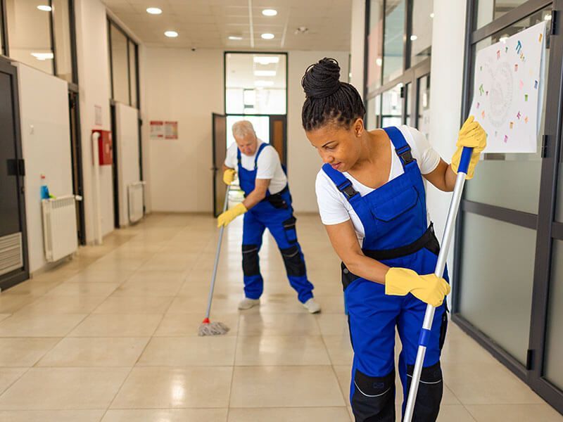 Two cleaners mopping a hallway in blue uniforms and yellow gloves