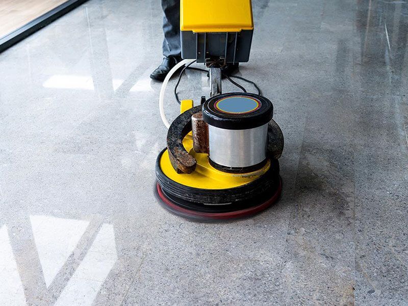 Floor polisher machine buffing a shiny gray concrete floor in an indoor space